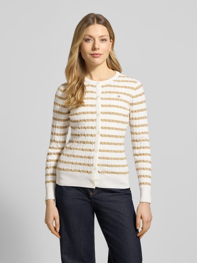 Frauenmodel trägt Strickjacke mit Baumwoll-Anteil von Gant, beige-weiß gestreift, Zopfmuster, Knopfleiste, körpernah, Ganzkörperansicht von vorne.