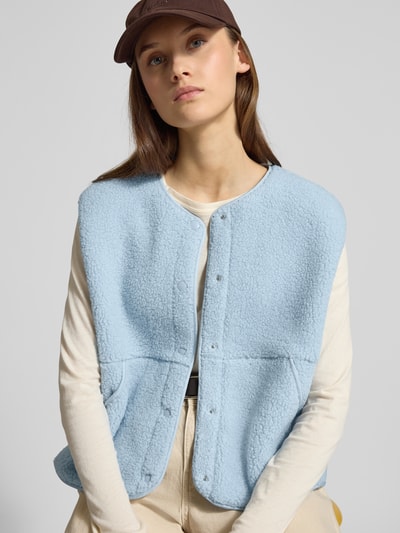 Frauenmodel trägt Relaxed Fit Weste in Teddy-Optik Modell 'Vera' von JJXX in Hellblau mit durchgängiger Knopfleiste, Rundhalsausschnitt und Eingrifftaschen, Struktur weich und wollig, Rückenlänge 54 cm, Schulterbreite 45 cm, Brustweite 58 cm, Nahaufnahme Oberkörper.