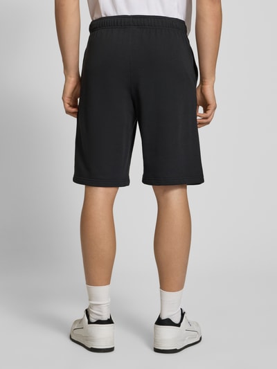 Männermodel trägt Shorts mit Logo-Print und -Stitching von CHAMPION, Baumwoll-Mix, lockerer Schnitt, schwarze Farbe, Ganzkörperansicht Rückansicht