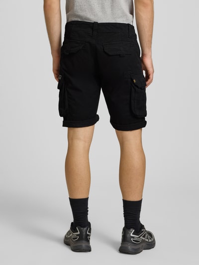 Mężczyznę model nosi szorty z kieszeniami cargo z mieszanki bawełny i elastanu model 'CREW SHORT' od Alpha Industries, krój regular fit, szerokość w rozmiarze 32: 44 cm, długość wewnętrzna nogawki w rozmiarze 32: 22 cm, czarny kolor, widok całej sylwetki z tyłu.