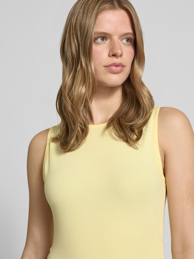 Frauenmodel trägt Top mit Rundhalsausschnitt Modell 'MOLLY' von Noisy May, Baumwoll-Elasthan-Mix, Slim-Fit, Label-Detail, Nahaufnahme Oberkörper. Rückenlänge bei Größe S: 52 cm. Pastellgelber Stoff mit glatter Textur.