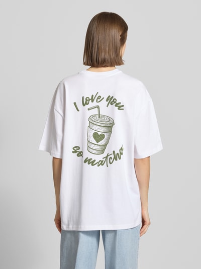 Frauenmodel trägt Oversized T-Shirt mit Statement-Print von REVIEW in Weiß aus Reine Baumwolle, Oversized-Fit, Rundhalsausschnitt, Rückenlänge 70 cm, Ganzkörperansicht Rückansicht.