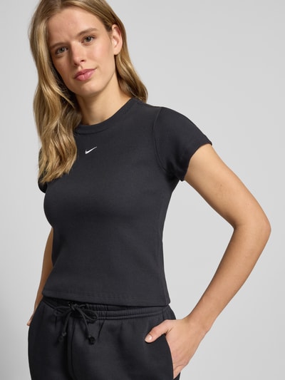 Frauenmodel trägt Cropped T-Shirt in Ripp-Optik mit Logo von Nike aus Baumwoll-Elasthan-Mix, Schwarz, Rundhalsausschnitt, Ganzkörperansicht von vorne. Rückenlänge bei Größe S: 48 cm.