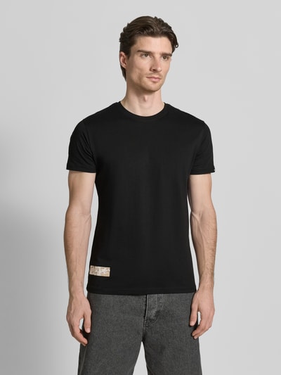 Männermodel trägt T-Shirt mit Label-Patch Modell 'Camo' von Alpha Industries in Schwarz, reine gewachste Baumwolle, Ganzkörperansicht von vorne.