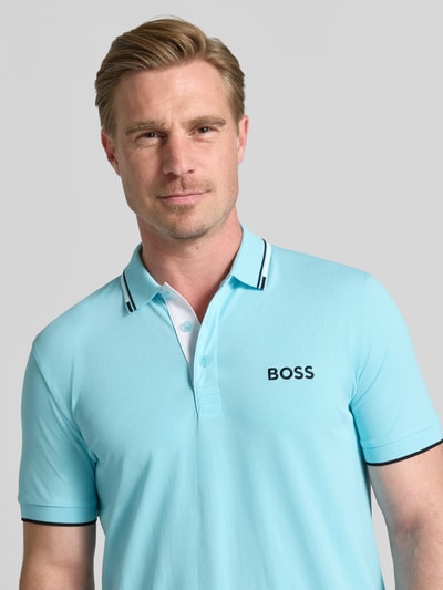 Mężczyzna nosi koszulkę polo Regular Fit Poloshirt aus Baumwoll-Mix model 'PADDY PRO' od BOSS Green w jasnoniebieskim kolorze z czarnymi detalami, tekstura gładka, logo na piersi, Nahaufnahme Oberkörper.