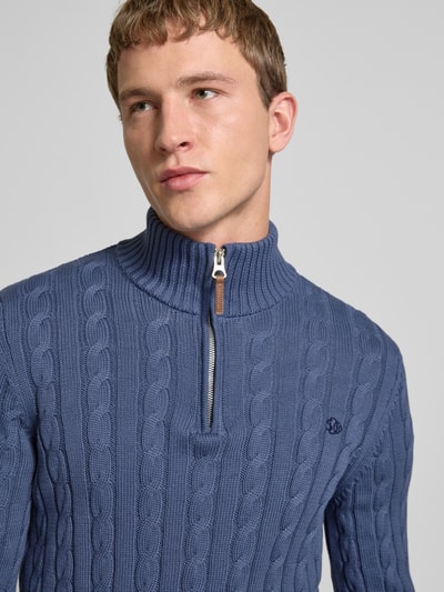Männermodel trägt Strickpullover aus reiner Baumwolle von Superdry in Blau mit Troyer-Kragen, Zopfmuster, Label-Detail, Nahaufnahme Oberkörper.