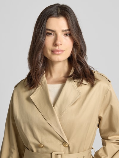 Frauenmodel trägt Cropped Trenchcoat mit Reverskragen Modell 'Fatou' von Guess aus beigem Baumwoll-Mix, doppelreihige Knopfleiste, Stoffgürtel, taillierte Passform, Nahaufnahme Oberkörper.