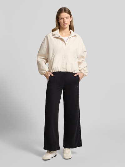 Vrouwenmodel draagt sweatpants met katoenmix model 'HER' van PUMA in zwart met wijd uitlopende pasvorm, zijzakken, labelstitching. Ganzekörperaanzicht van voren.
