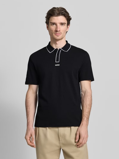 Männermodel trägt Regular Fit Poloshirt aus reiner Baumwolle Modell 'DALUMO' von HUGO in Schwarz, Label-Schriftzug, Ganzkörperansicht von vorne.