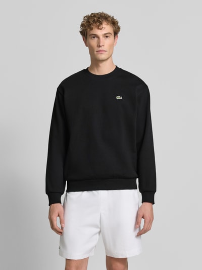 Männermodel trägt schwarzes Regular Fit Sweatshirt aus Baumwoll-Mix von Lacoste, glatte Struktur, weiße Shorts, Ganzkörperansicht von vorne. Herren Sweatshirt von Lacoste