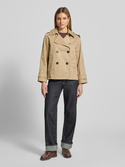 Frauenmodel trägt Trenchcoat mit Logo-Muster von MICHAEL Michael Kors, beiger Zweireiher mit Reverskragen und Ärmelriegel, Regular-Fit, Ganzkörperansicht von vorne. Rückenlänge bei Größe S: 65 cm, Schulterbreite: 48 cm, Brustweite: 53 cm, Ärmellänge: 57 cm.