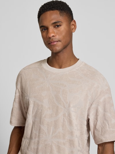 Männermodel trägt Regular Fit T-Shirt aus Baumwoll-Mix Modell 'TE_FLOWER' von BOSS Orange mit Optik: Allover-Muster, Struktur, Label-Applikation, Rundhals, Kurzarm, Materialverarbeitung: Frottee, Nahaufnahme Oberkörper.