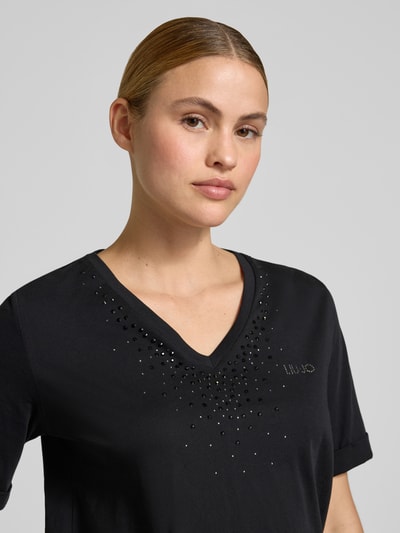 Frauenmodel trägt T-Shirt mit Strasssteinbesatz und V-Ausschnitt von LIU JO SPORT, schwarzer Baumwollstoff, Nahaufnahme Oberkörper.