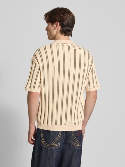Männermodel trägt Regular Fit Strick-Poloshirt Modell 'POUL' von Redefined Rebel aus Baumwoll-Mix, creme mit dunklen Streifen, Ganzkörperansicht Rückansicht. Rückenlänge bei Größe M: 66 cm, Knopfleiste am Kragen.
