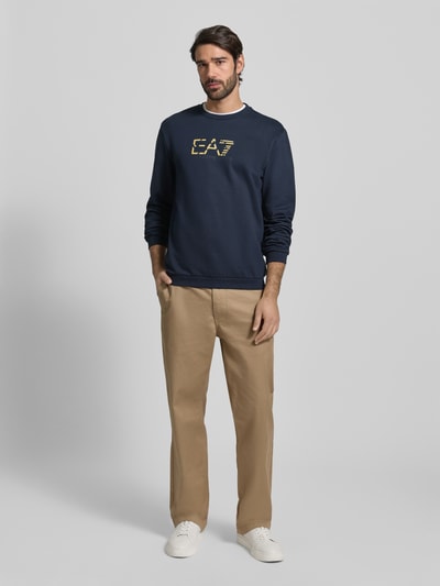 Männermodel trägt Sweatshirt mit Logo und Rundhalsausschnitt von EA7 Emporio Armani in Dunkelblau, reine Baumwolle, Regular Fit, Ganzkörperansicht von vorne.