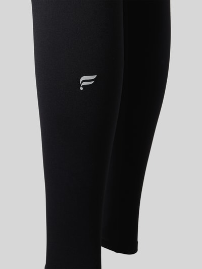 Frauenmodel trägt schwarze Leggings mit elastischem Bund und Label-Detail von Fabletics, Material-Mix mit Stretch-Anteil, Nahaufnahme Bein.