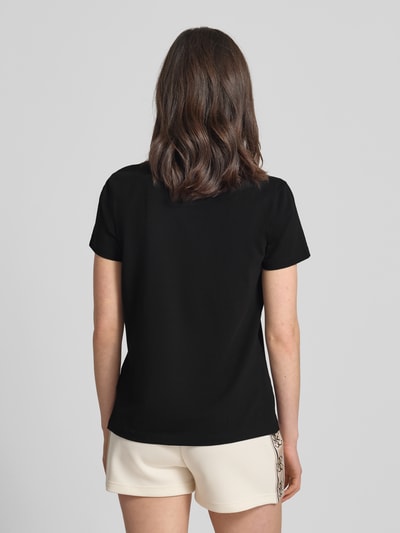 Frauenmodel trägt Regular Fit T-Shirt mit Logo-Applikation Modell 'Colette' von Guess Activewear aus elastycznego bawełnianego materiału, czarny kolor, gładka tekstura, klasyczny okrągły dekolt, plecy długości 60 cm w rozmiarze S, Ganzkörperansicht Rückansicht.