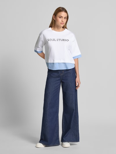 Kobiece modelka nosi damski t-shirt z cekinowym obszyciem i okrągłym dekoltem od Smith and Soul, bawełna, pudełkowy krój, długość tyłu 54 cm, widok całej sylwetki z przodu.
