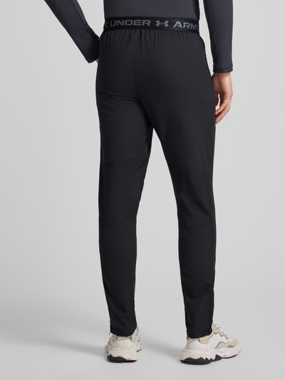 Männermodel draagt Trainingshose mit Reißverschlusstaschen van Under Armour, regular fit, elastische band, model Vanish Woven Tapered Pant, ritszakken, binnenbeenlengte maat M 84 cm, zwarte kleur, gladde stofstructuur, Ganzkörperansicht Rückansicht.