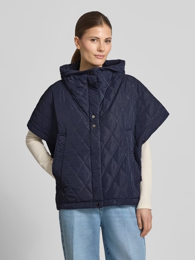 Frauenmodel trägt Cape mit Steppnähten und Eingrifftaschen von Copenhagen Muse, dunkelblau, Relaxed-Fit, ganzkörperansicht von vorne. Rückenlänge bei Größe S/M: 66 cm, Schulterbreite: 42 cm, Brustweite: 25 cm, hochgeschlossener Kragen, Knopfleiste.