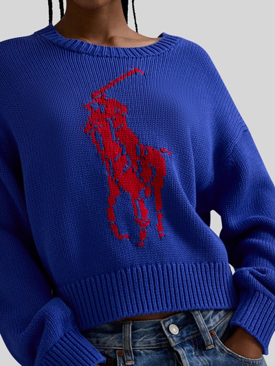 Frauenmodel trägt Regular Fit Strickpullover aus reiner Baumwolle von Polo Ralph Lauren in Blau mit rotem Two Tone Pony-Intarsia, Nahaufnahme Oberkörper.