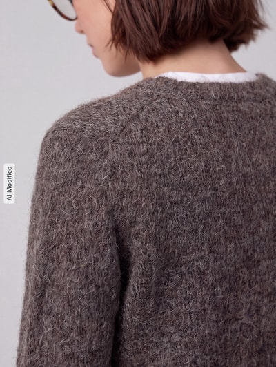 Frauenmodel trägt Regular Fit Strickjacke mit Woll-Anteil Modell 'NOVAH' von VERO MODA, braune grobe Stricktextur, Nahaufnahme Rücken, KI-modifiziertes Bild.