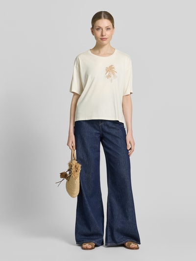 Frauenmodel trägt Damen T-Shirt mit Motiv-Stitching von Fynch-Hatton in Beige, Baumwoll-Mix mit Modal-Anteil, Loose-Fit, Rundhalsausschnitt, kombiniert mit blauen Jeans, Rückenlänge bei Größe S 58 cm, Ganzkörperansicht von vorne.