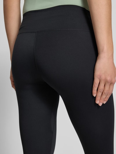 Frauenmodel trägt Tights mit elastischem Bund und Logo von NIKE TRAINING, schwarzer Material-Mix mit Stretch, Nahaufnahme Rückansicht.