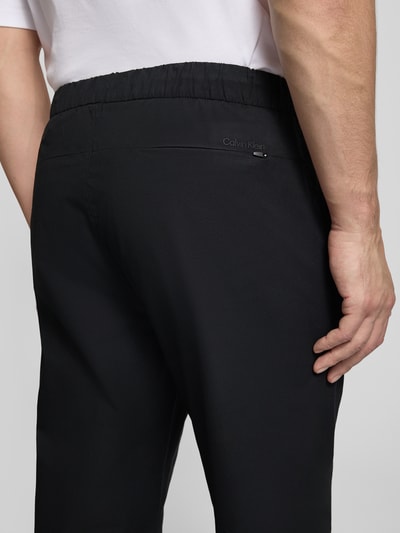 Männermodel trägt Slim Fit Schlupfhose mit Gesäßtasche von CK Calvin Klein in Schwarz, elastischer Bund, Detailaufnahme Rückansicht.