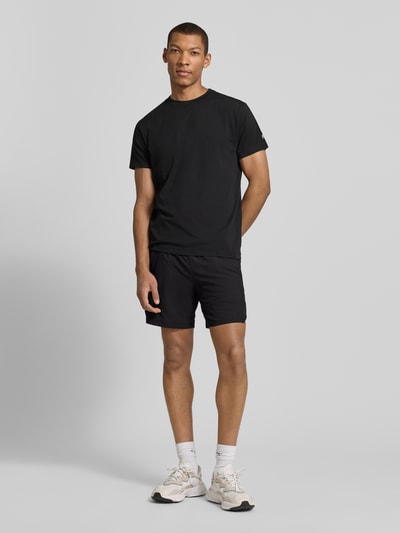 Męski model nosi Regular Fit T-Shirt mit Logo-Print von Fabletics, bawełniany miks, czarny, okrągły dekolt, długość tyłu M: 65 cm, Ganzkörperansicht von vorne.
