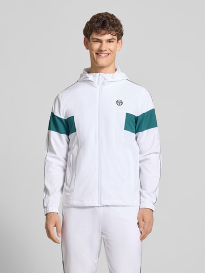 Männermodel trägt weiße Regular Fit Jacke mit grünem Einsatz und Logo-Stitching Modell 'Caspio' von SERGIO TACCHINI, Ganzkörperansicht von vorne. Elastischer Material-Mix, Kapuze mit Tunnelzug, Reißverschluss, Eingrifftaschen und elastische Ärmelabschlüsse.