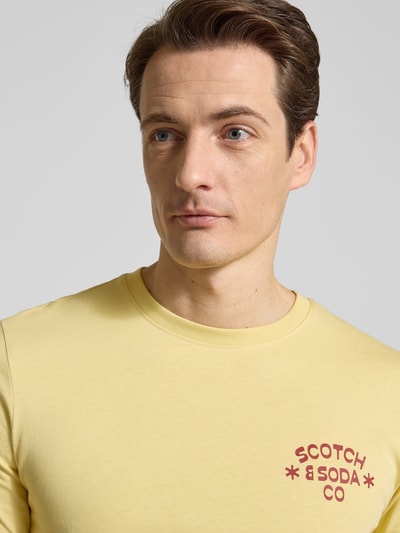 Męski model nosi T-shirt mit Rundhalsausschnitt von Scotch & Soda z bawełny, krój regular fit, nadruk z logo, okrągły dekolt, długość tyłu 68 cm w rozmiarze M, zbliżenie na górną część ciała.