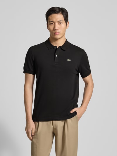 Männermodel trägt Regular Fit Poloshirt aus reiner Baumwolle von Lacoste, Optik: Unifarben, Logo-Detail, Ganzkörperansicht von vorne.
