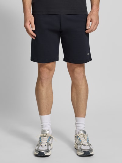 Männermodel trägt Sweatshorts mit Eingrifftaschen von Christian Berg Men aus Reine Baumwolle, Regular-Fit, Label-Detail, Ganzkörperansicht von vorne.