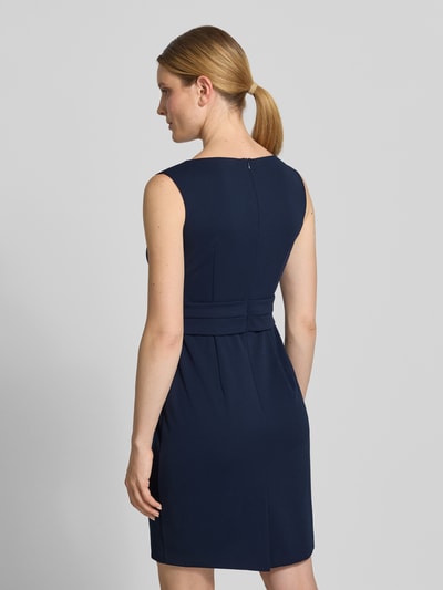 Frauenmodel trägt knielanges Cocktailkleid mit Knotendetail von Vera Mont, dunkelblauer Material-Mix, gerader Schnitt, Ganzkörperansicht Rückansicht.