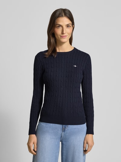 Frauenmodel trägt Strickpullover mit Label-Detail von GANT aus Baumwoll-Mix mit Stretch-Anteil im unifarbenen Design, Strukturmuster, Rundhalsausschnitt und gerippten Abschlüssen, körpernaher Schnitt, Ganzkörperansicht von vorne.