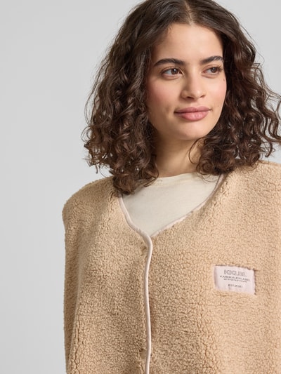 Frauenmodel trägt Fleeceweste mit Label-Detail von Karo Kauer in Beige, Relaxed-Fit, V-Ausschnitt, Knopfleiste, Nahaufnahme Oberkörper. Rückenlänge bei Größe S: 70 cm, Schulterbreite: 48 cm, Brustweite: 61 cm.
