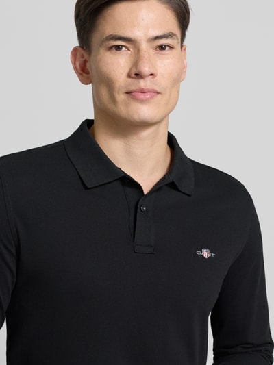 Męski model nosi Regular Fit Poloshirt mit Label-Stitching od Gant, czarna bawełna, kołnierzyk, logowanie, zbliżenie na górę ciała.