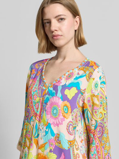 Frauenmodel trägt Knielanges Kleid aus Viskose mit Tunikakragen von Emily Van den Bergh, buntes Muster, Nahaufnahme Oberkörper. Gerade Passform, reine Viskose, 3/4-Arm, Farben: Lila, Gelb, Rosa, Blau.