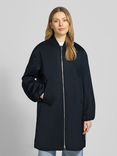 Kobieta modelka nosi Regular Fit Blouson-Mantel mit College-Kragen od Marc O'Polo, efekt: jednolity kolor, krój regular fit, kołnierz college, zamek błyskawiczny dwustronny, naszywka z logo, długi rękaw z elastycznym wykończeniem, wpuszczane kieszenie boczne, kieszeń wewnętrzna, wykończenie materiału: satyna; pełny widok z przodu.
