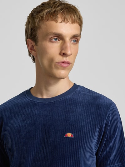 Męski model nosi t-shirt z mieszanki bawełny od Ellesse, krój regular fit, okrągły dekolt, logo, model 'MADORI', z dodatkiem streczu, długość tyłu w rozmiarze m: 66 cm, granatowy, prążkowana faktura, miękka struktura, nahaufnahme oberkörper.
