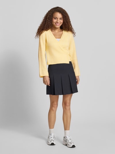 Frauenmodel trägt Regular Fit Strickjacke mit Woll-Anteil Modell 'COLO' von Only, Melange-Optik, Wickeloptik, gelb, Ganzkörperansicht von vorne.