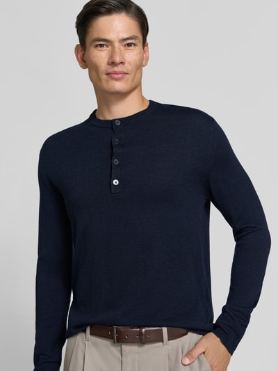 Männermodel trägt Strickpullover mit Henley-Kragen von DRYKORN in Dunkelblau, reine Baumwolle, gerader Schnitt, Nahaufnahme Oberkörper.