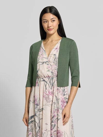 Frauenmodel trägt Regular Fit Bolero aus Viskose-Mix von Vera Mont in Olivgrün zu cremefarbenem Kleid mit Blumenmuster, Ganzkörperansicht von vorne, Damen Bolero von Vera Mont.