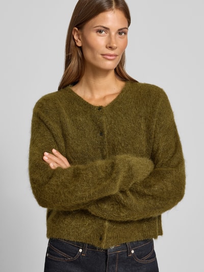 Frauenmodel trägt Strickjacke aus Woll-Mohair-Mix Modell 'debbie' von Gestuz in Olivgrün, weiche Textur, Knopfleiste, Nahaufnahme Oberkörper. Lockere Passform, gerippte Abschlüsse, Stretch-Anteil, Rückenlänge 41 cm, Ärmellänge 65 cm.