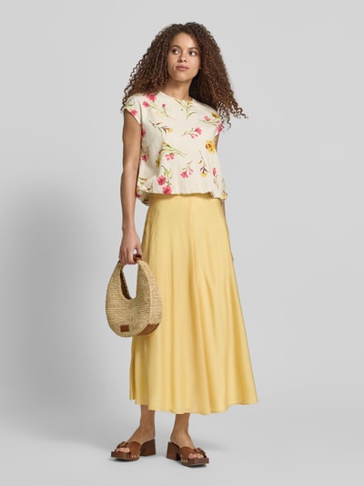 Vrouwenmodel draagt Midirock mit rückseitigem Reißverschluss van Jake*s Collection uit satijn in A-lijn, zachtgeel, glanzende textuur, volledige lichaamsaanzicht van voren.