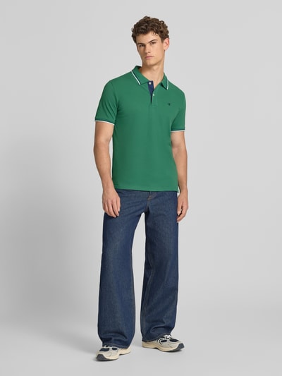 Mannelijk model draagt Slim Fit Poloshirt met Label-Stitching van CHAMPION in groen, puur katoen, knoopsluiting, ruglengte maat M 73 cm, ganzlichaamsaanzicht van voren.