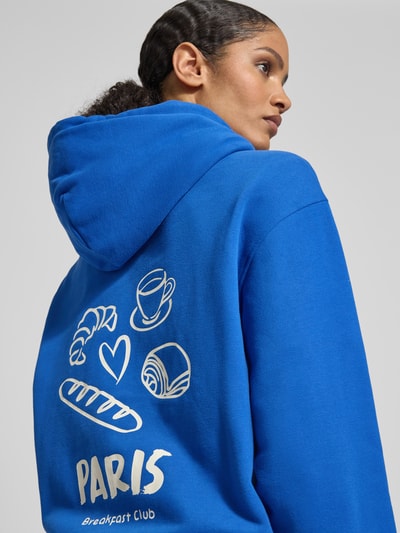 Frauenmodel trägt blaue Sweatjacke mit Zweiwege-Reißverschluss von Smith and Soul, Kapuze, Print und Label-Detail, Ganzkörperansicht Rückansicht.