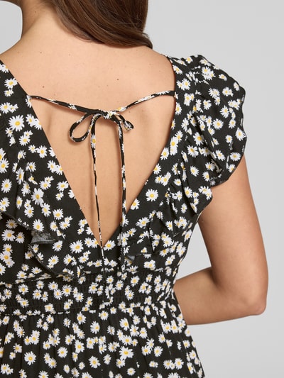 Frauenmodel trägt Leicht ausgestelltes Maxikleid aus reiner Viskose Modell 'EASY JOY' von Vero Moda mit Allover-Blumenmuster, tiefem V-Rückenausschnitt, Rüschen, Gummizug, Bindeverschluss; Nahaufnahme Rücken.