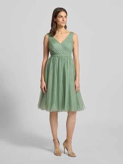 Frauenmodel trägt Cocktailkleid mit V-Ausschnitt von TROYDEN COLLECTION in Unifarben, taillierter Schnitt, Ganzkörperansicht von vorne.